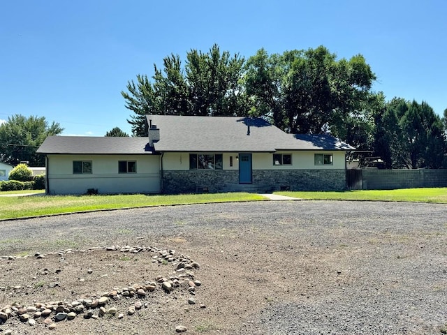 ranch-style house with stone siding, driveway, a front lawn, and fence