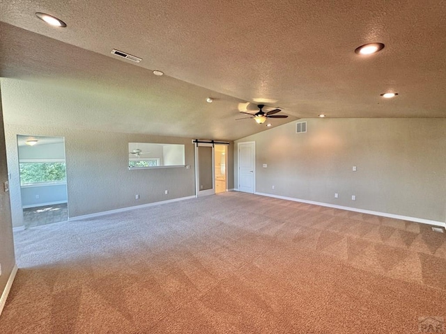 carpeted spare room with lofted ceiling, visible vents, ceiling fan, and a barn door