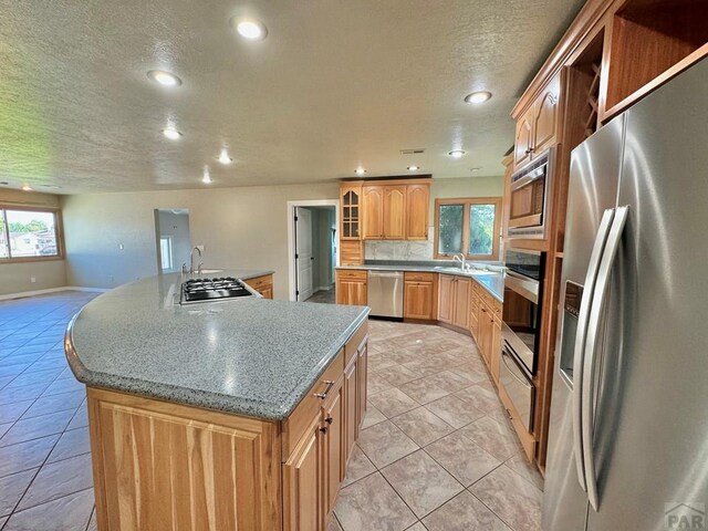 kitchen with light tile patterned floors, stainless steel appliances, an island with sink, and glass insert cabinets