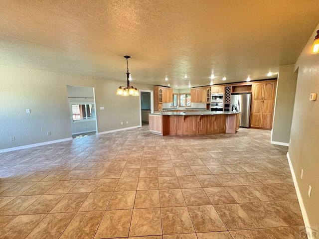 kitchen with brown cabinetry, appliances with stainless steel finishes, light countertops, a chandelier, and pendant lighting