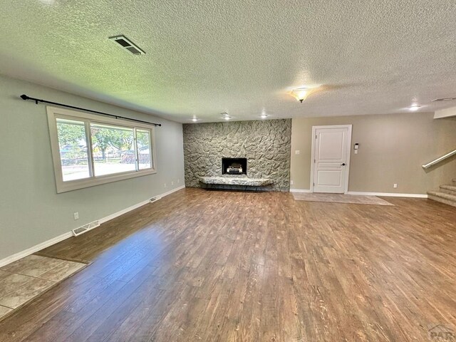 unfurnished living room featuring a stone fireplace, stairway, wood finished floors, and visible vents