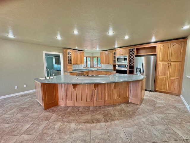 kitchen with stainless steel appliances, a large island with sink, glass insert cabinets, and a sink