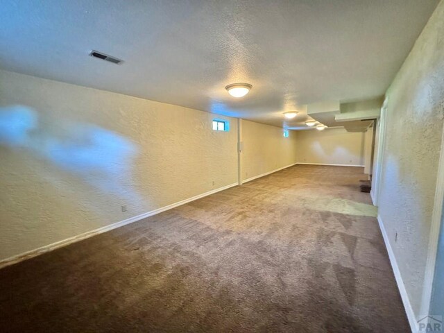 finished below grade area with a textured ceiling, a textured wall, visible vents, baseboards, and carpet