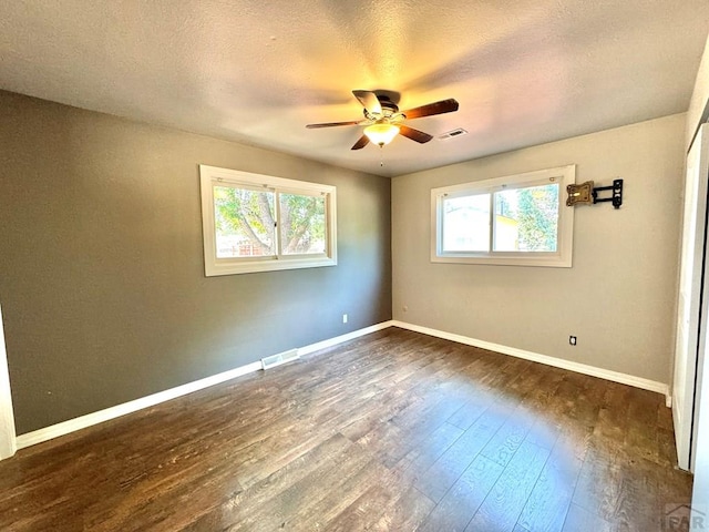 spare room featuring a healthy amount of sunlight, dark wood-style floors, and visible vents