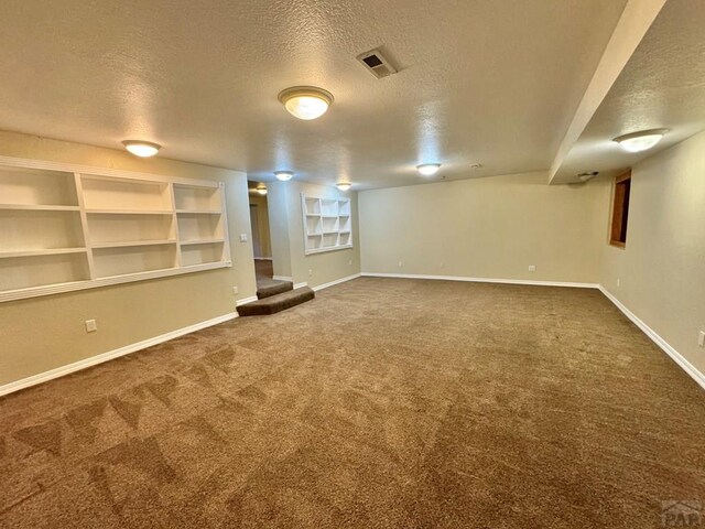 finished below grade area with carpet floors, visible vents, a textured ceiling, and baseboards