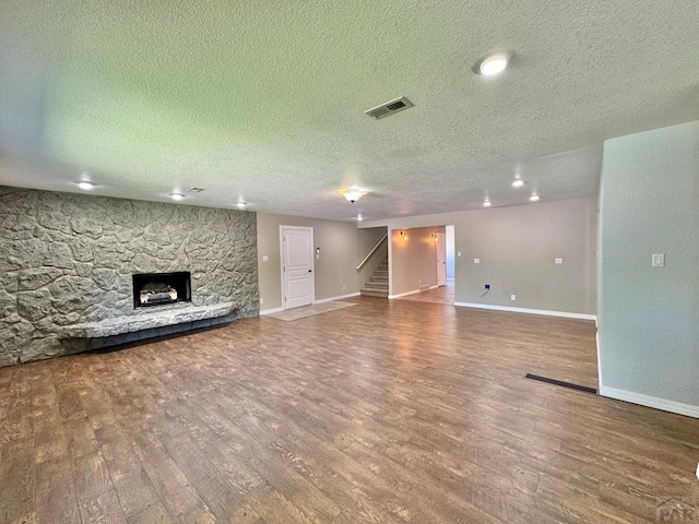 unfurnished living room featuring a stone fireplace, stairway, wood finished floors, and visible vents