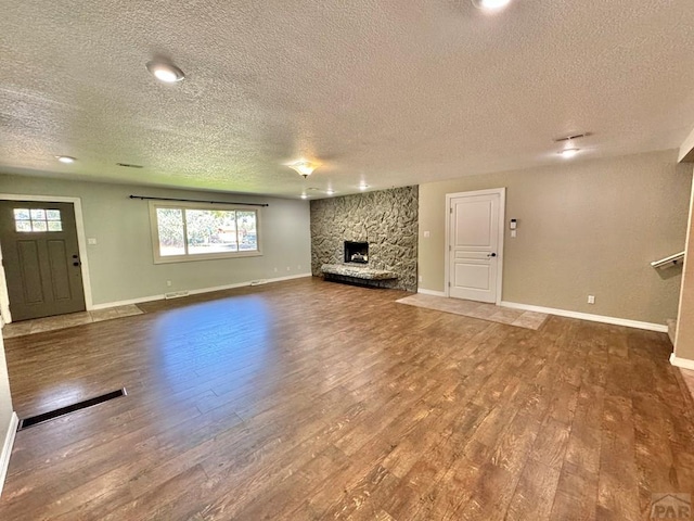 unfurnished living room featuring visible vents, baseboards, wood finished floors, and a stone fireplace