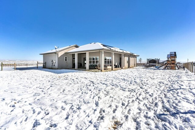 snow covered house with a playground, fence, and stucco siding