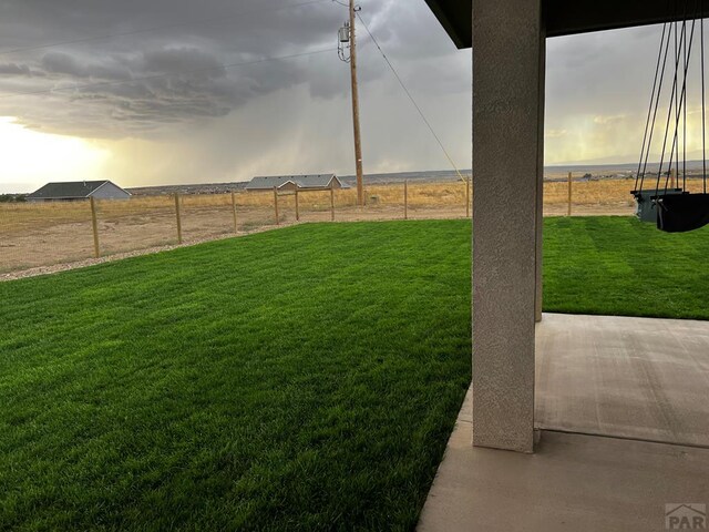 yard at dusk with a rural view, a patio, and fence