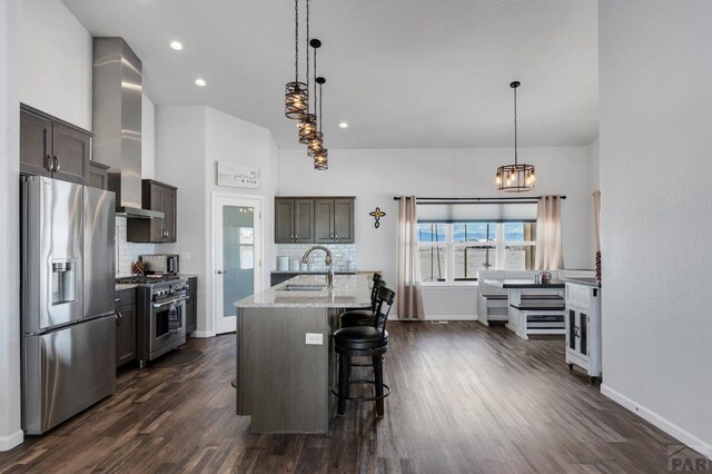 kitchen featuring light stone counters, stainless steel appliances, a sink, hanging light fixtures, and a center island with sink