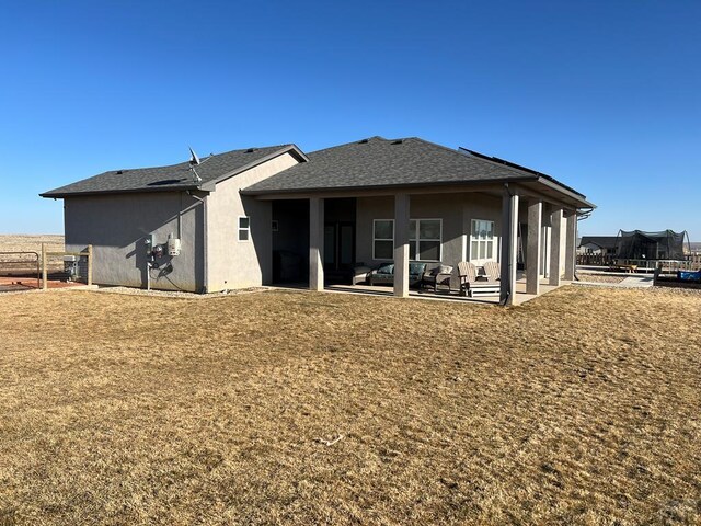 back of house featuring a shingled roof, a lawn, stucco siding, a trampoline, and a patio area