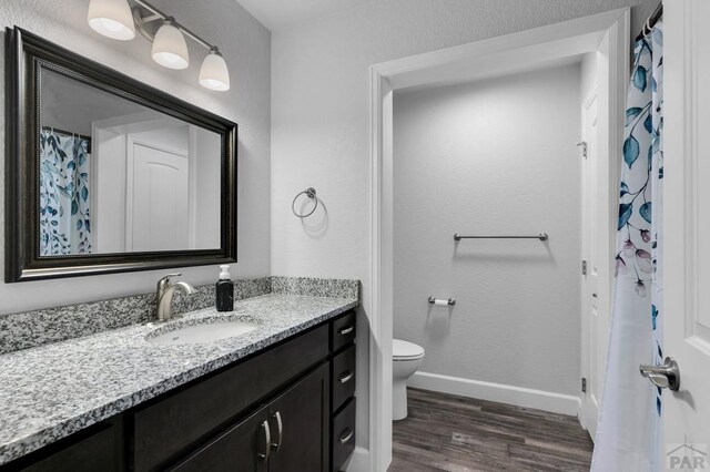 bathroom with toilet, wood finished floors, vanity, and baseboards