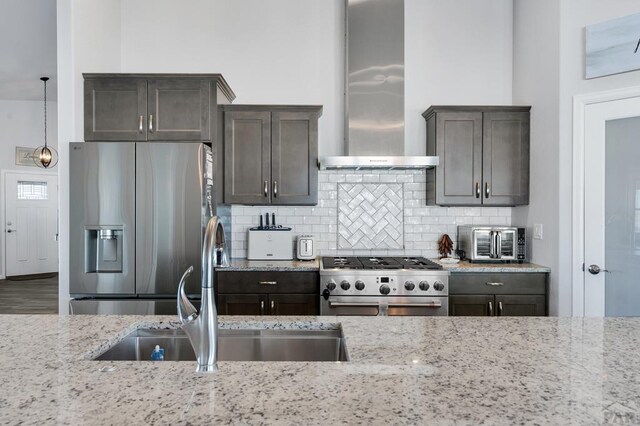 kitchen with range, stainless steel fridge with ice dispenser, light stone counters, decorative light fixtures, and wall chimney range hood