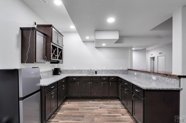 kitchen featuring a peninsula, light wood-style flooring, freestanding refrigerator, and light stone countertops