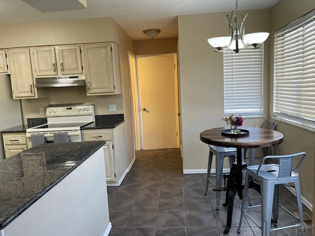 kitchen with under cabinet range hood, hanging light fixtures, white range with electric stovetop, dark stone counters, and an inviting chandelier