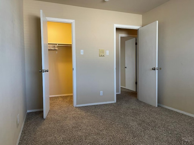 unfurnished bedroom with carpet floors, a spacious closet, baseboards, and a closet