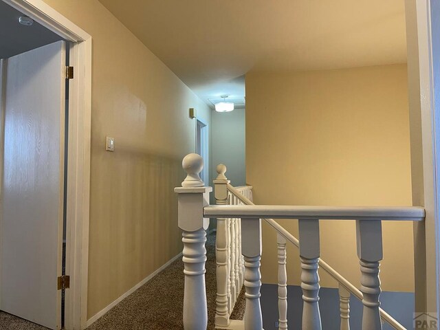 hall featuring baseboards, carpet flooring, and an upstairs landing