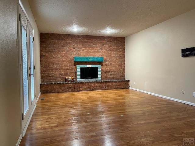 unfurnished living room featuring a brick fireplace, a textured ceiling, baseboards, and wood finished floors