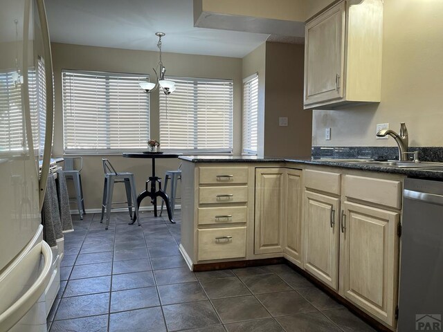 kitchen featuring dark tile patterned floors, a sink, hanging light fixtures, dishwasher, and dark countertops