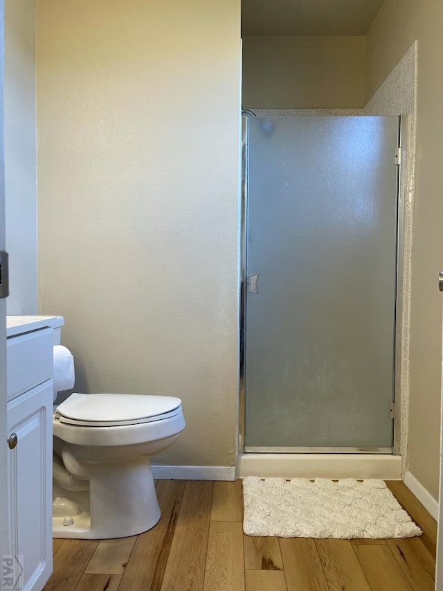 bathroom with toilet, wood finished floors, vanity, baseboards, and a stall shower