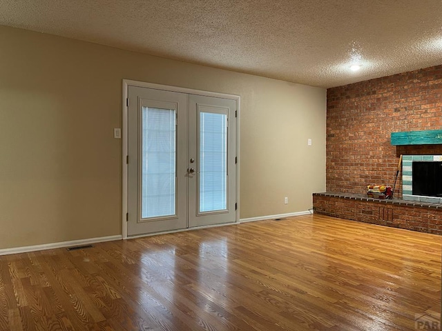 unfurnished living room featuring french doors, a fireplace, a textured ceiling, wood finished floors, and baseboards