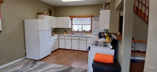 kitchen with light countertops, light wood-style flooring, white cabinets, a sink, and white appliances