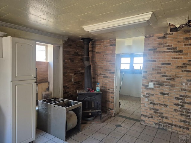 interior space with a wood stove, brick wall, white cabinets, and light tile patterned flooring