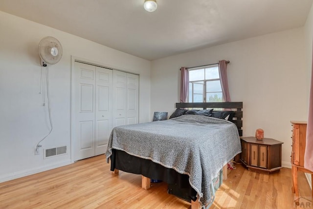 bedroom with light wood-style floors, baseboards, visible vents, and a closet