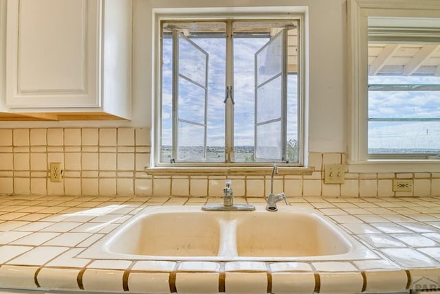 room details with tasteful backsplash, white cabinetry, a sink, and tile countertops