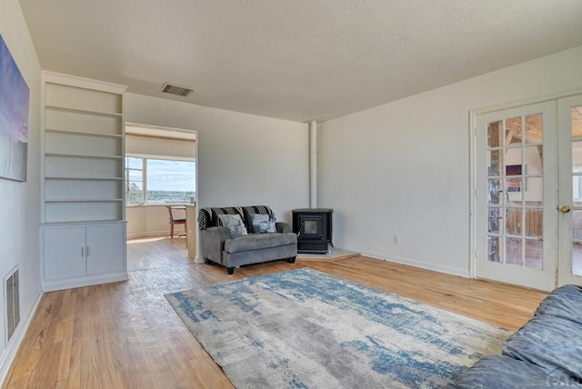 living area featuring visible vents, wood finished floors, a wood stove, a textured ceiling, and french doors