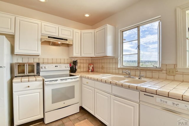 kitchen with under cabinet range hood, tile counters, white appliances, and a sink