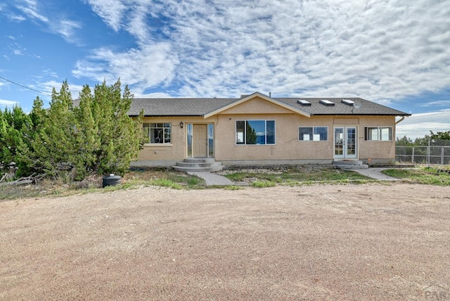 view of front of property featuring french doors, roof with shingles, fence, and stucco siding