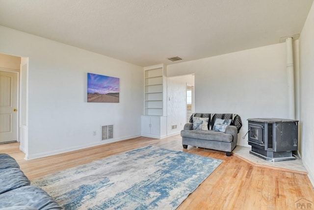 living area featuring a wood stove, built in shelves, visible vents, and wood finished floors