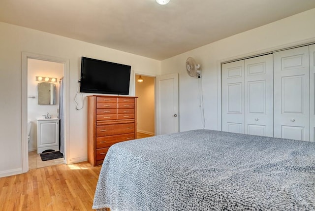 bedroom featuring a closet, baseboards, ensuite bath, light wood-type flooring, and a sink