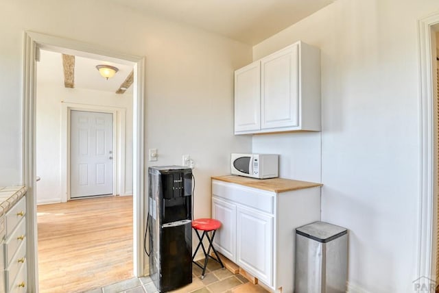 kitchen with butcher block counters, white cabinetry, light wood finished floors, and white microwave