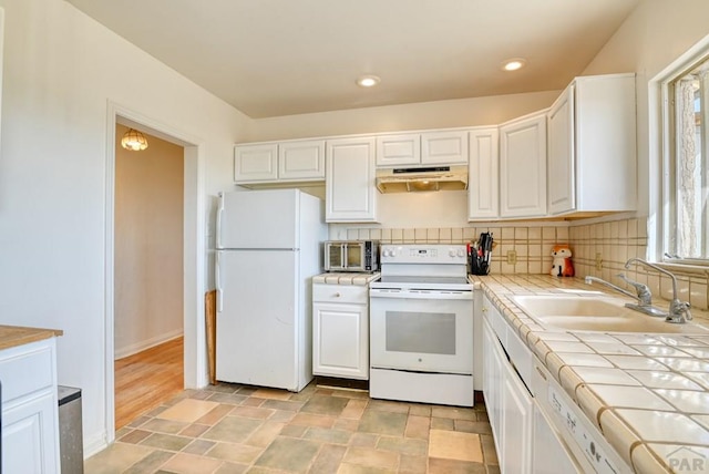 kitchen with under cabinet range hood, white appliances, a sink, white cabinets, and tile counters