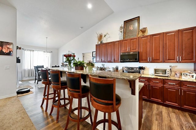 kitchen featuring a center island, a breakfast bar, stainless steel appliances, high vaulted ceiling, and light stone counters