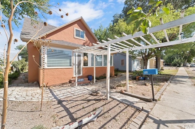 rear view of property featuring entry steps, a shingled roof, a pergola, and stucco siding