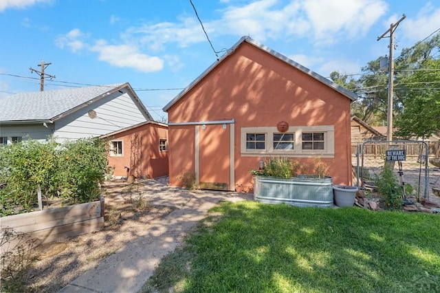 back of house with an outdoor structure, fence, a garden, a yard, and stucco siding