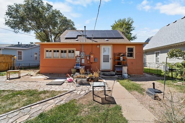 back of house featuring entry steps, roof mounted solar panels, fence, and stucco siding