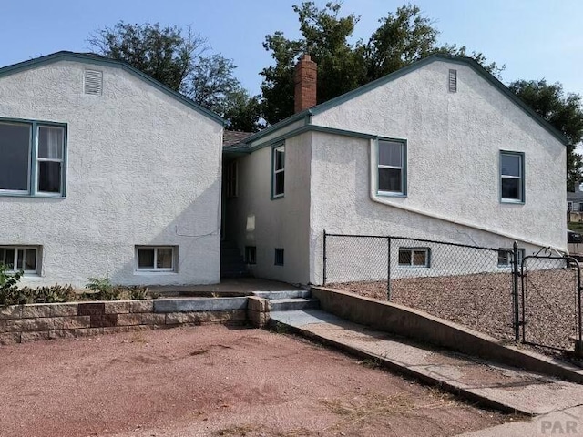 back of house featuring a chimney, fence, and stucco siding