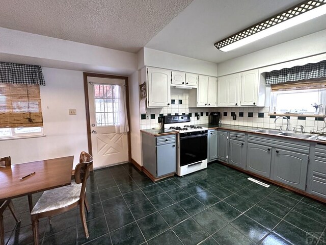 kitchen featuring tasteful backsplash, white range with gas stovetop, white cabinets, gray cabinetry, and a sink