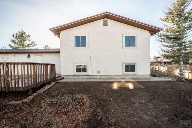 back of house with fence, a wooden deck, and stucco siding