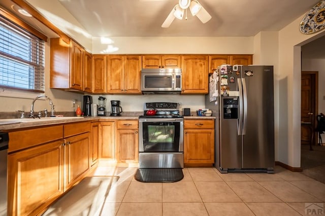 kitchen with light tile patterned flooring, stainless steel appliances, a sink, a ceiling fan, and brown cabinetry