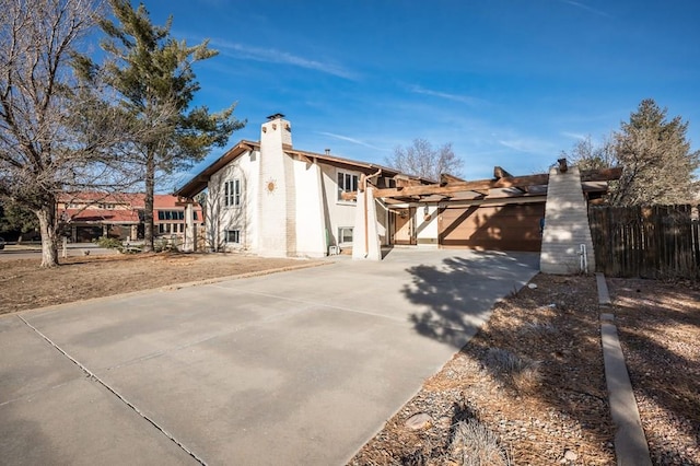 view of side of property with a chimney, fence, and concrete driveway