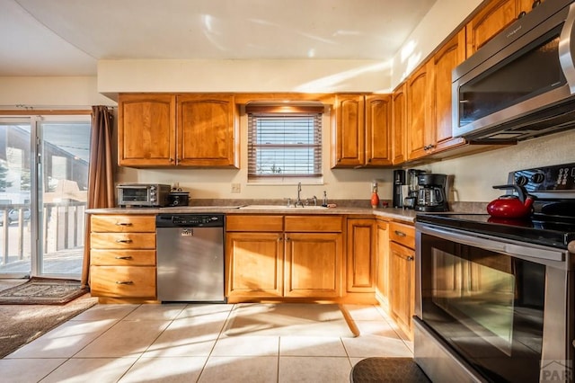 kitchen featuring a toaster, brown cabinets, stainless steel appliances, light tile patterned flooring, and a sink