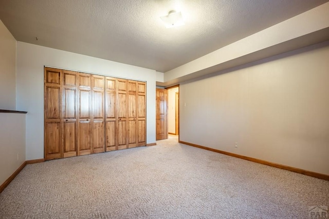 unfurnished bedroom with light carpet, a closet, baseboards, and a textured ceiling