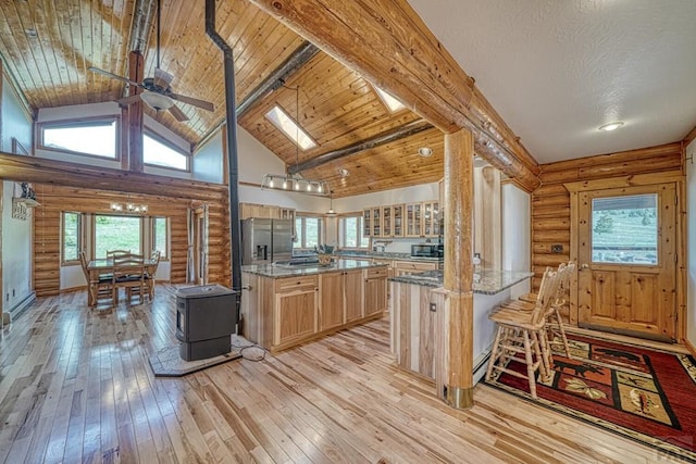 kitchen with a kitchen island, light stone counters, light wood-type flooring, light brown cabinets, and high vaulted ceiling