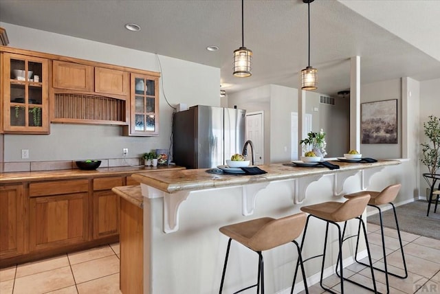 kitchen featuring a breakfast bar, freestanding refrigerator, light tile patterned flooring, brown cabinetry, and light countertops