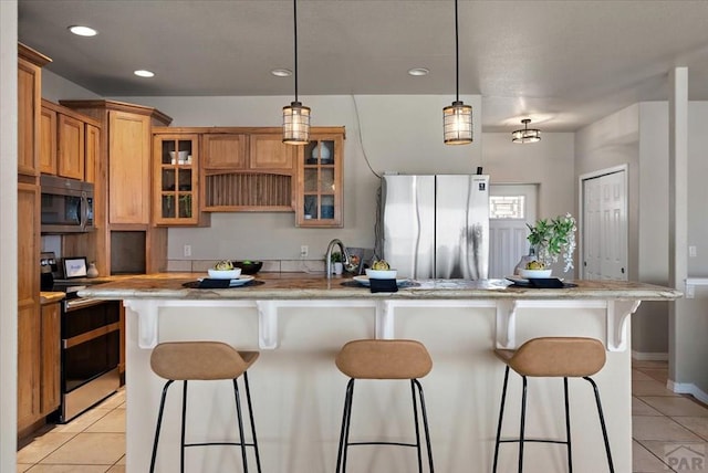 kitchen with light tile patterned floors, a center island with sink, appliances with stainless steel finishes, and a kitchen bar